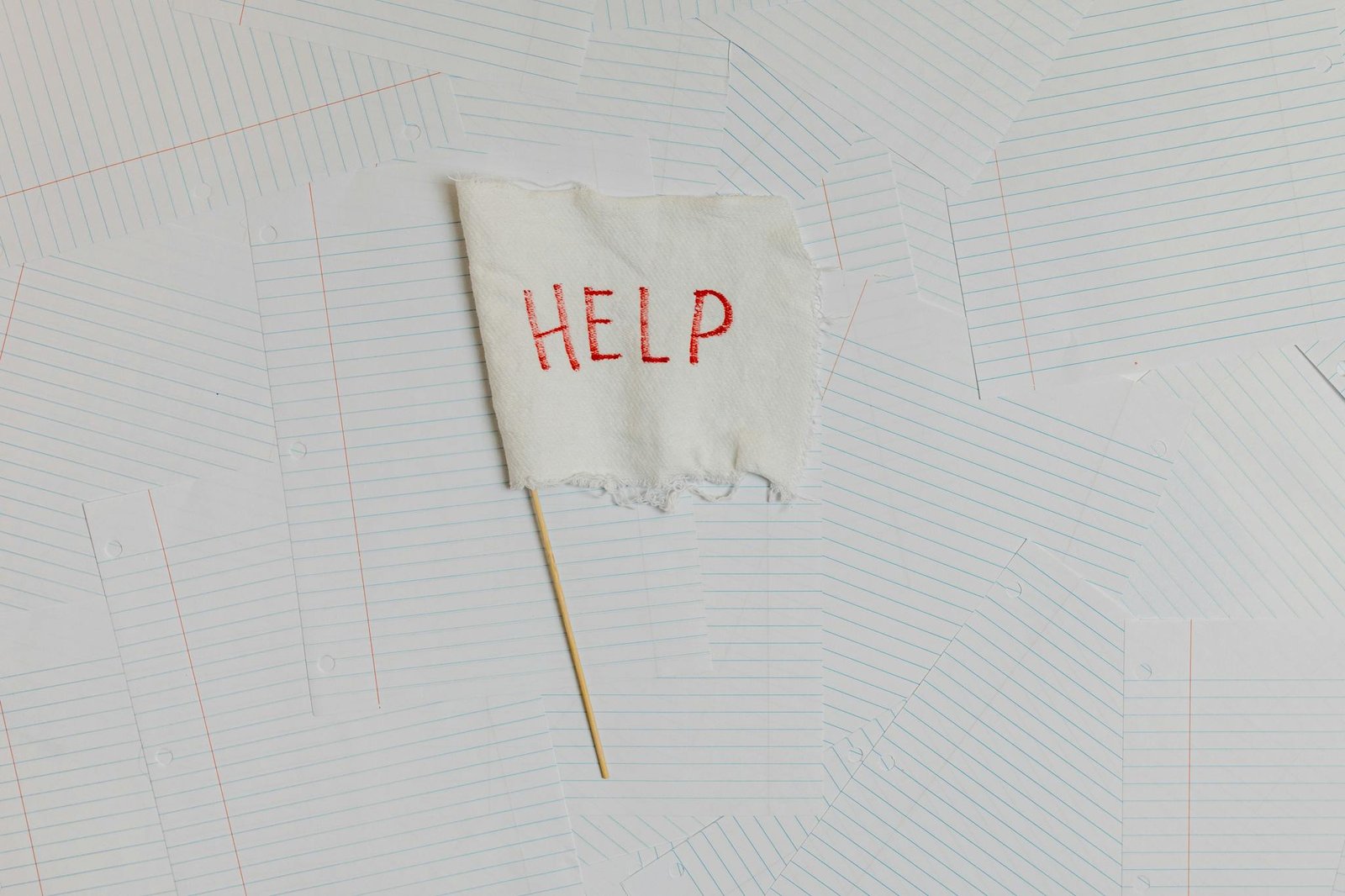 A fabric flag with 'HELP' on a scattered notepaper background, symbolizing distress or overwhelm.
