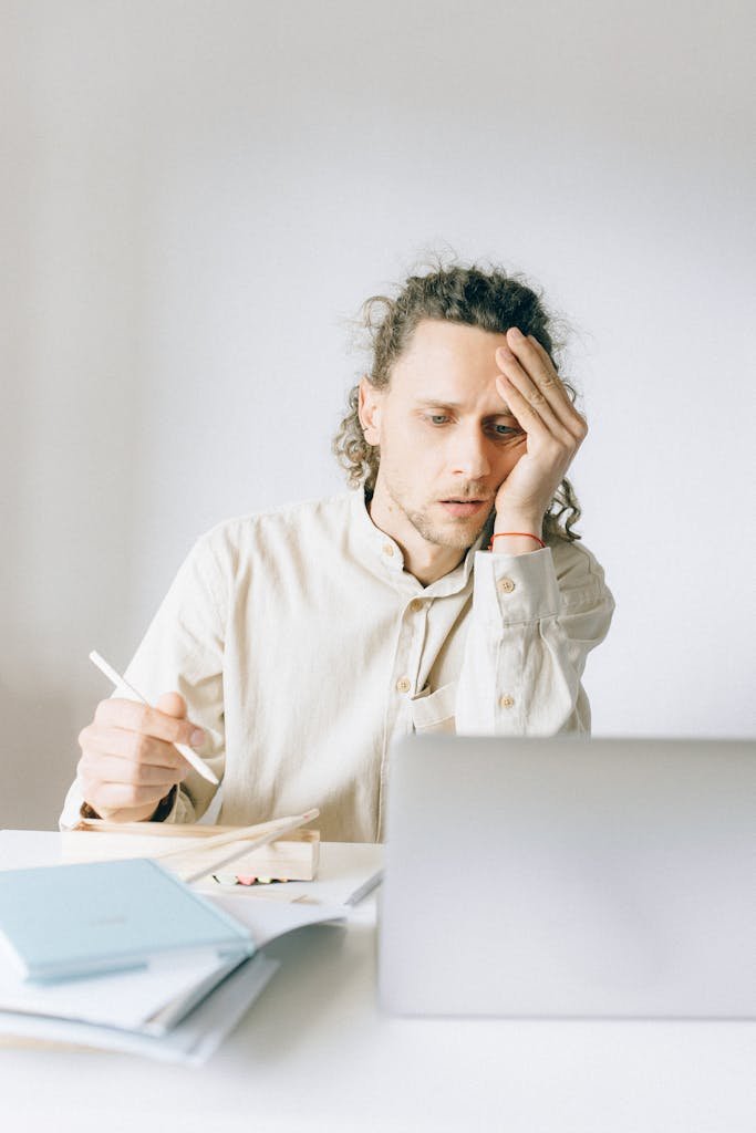 Young man overwhelmed by work at his desk, showing stress and fatigue.