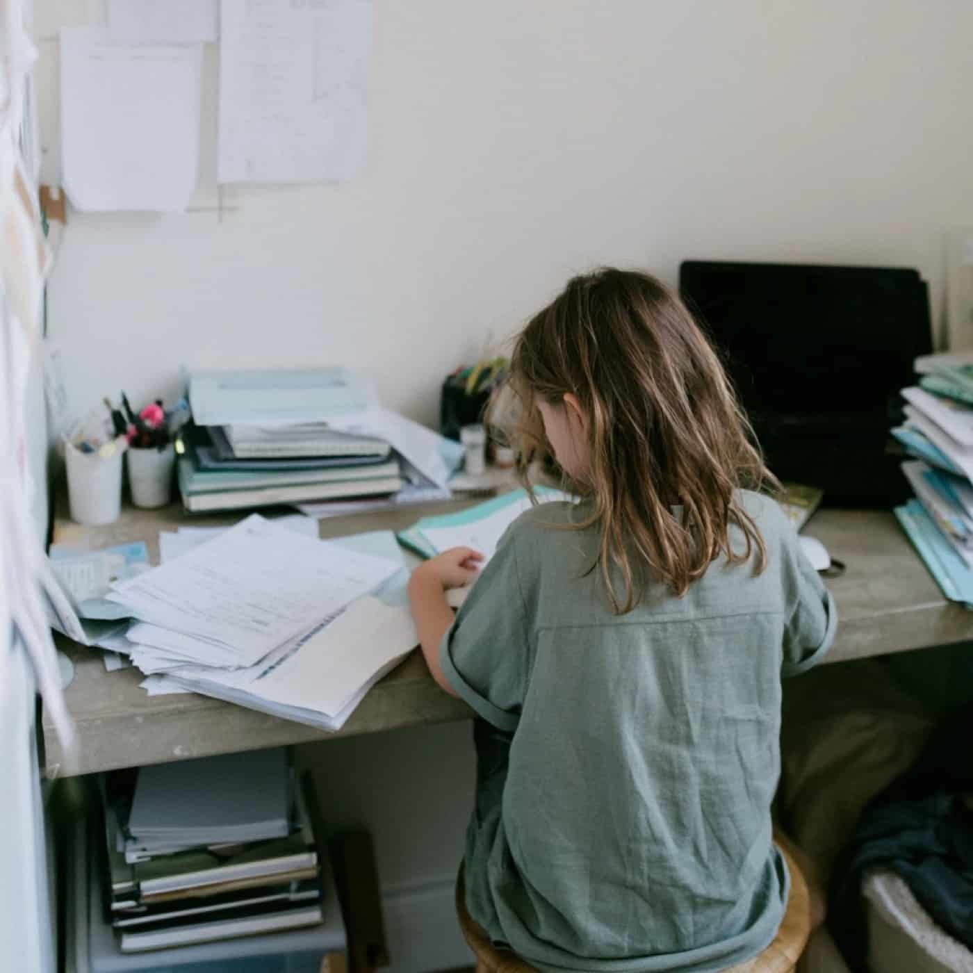 Une petite fille seule à son bureau couvert de feuilles