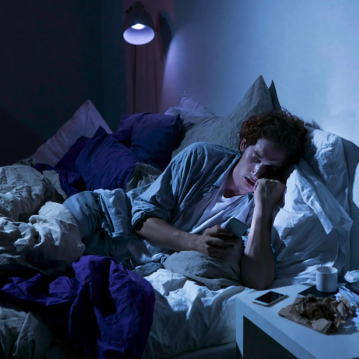 Un homme réveillé en pleine nuit dans son lit, son téléphone à la main