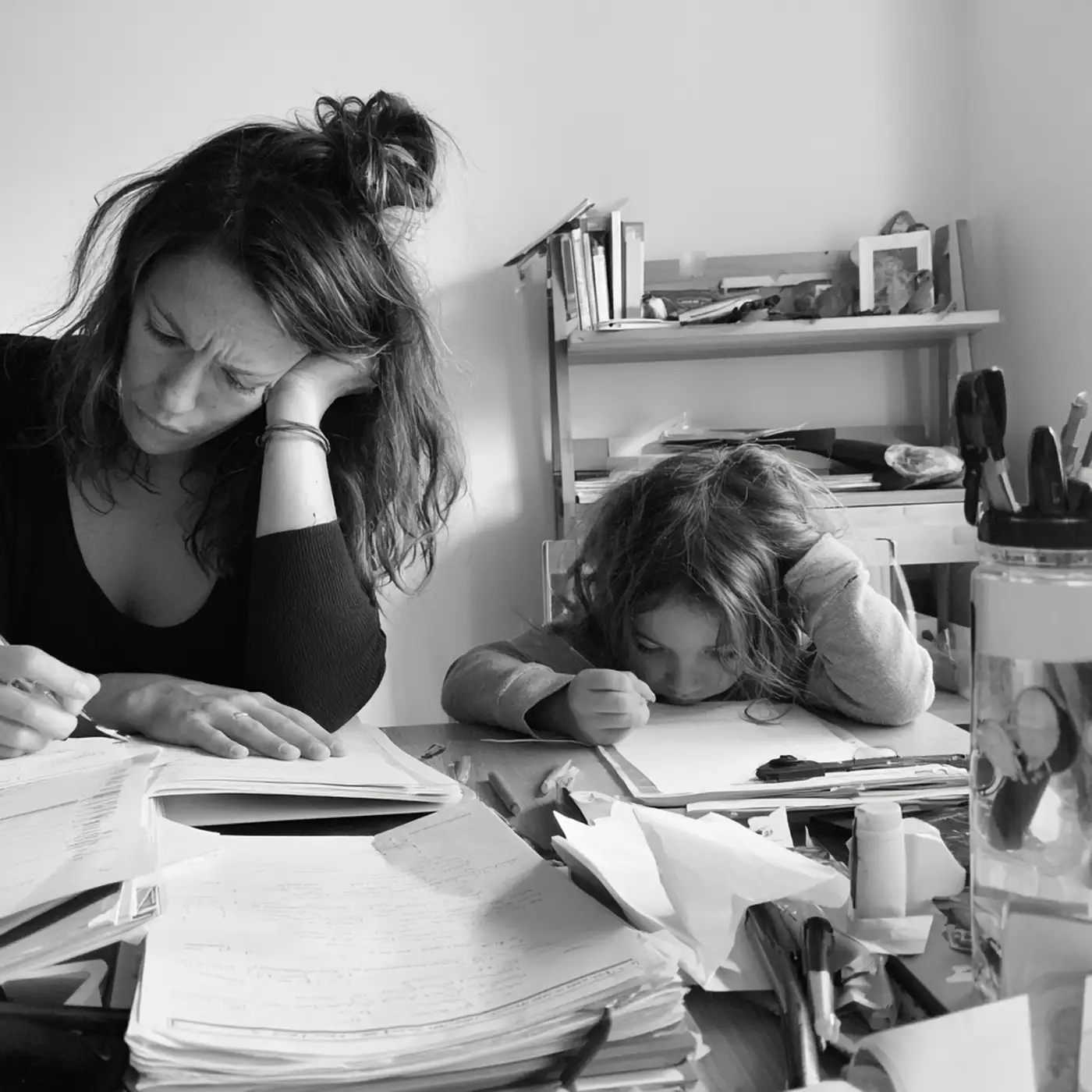 Une maman épuisée, la tête dans la main, à côté de son enfant penché sur ses devoirs