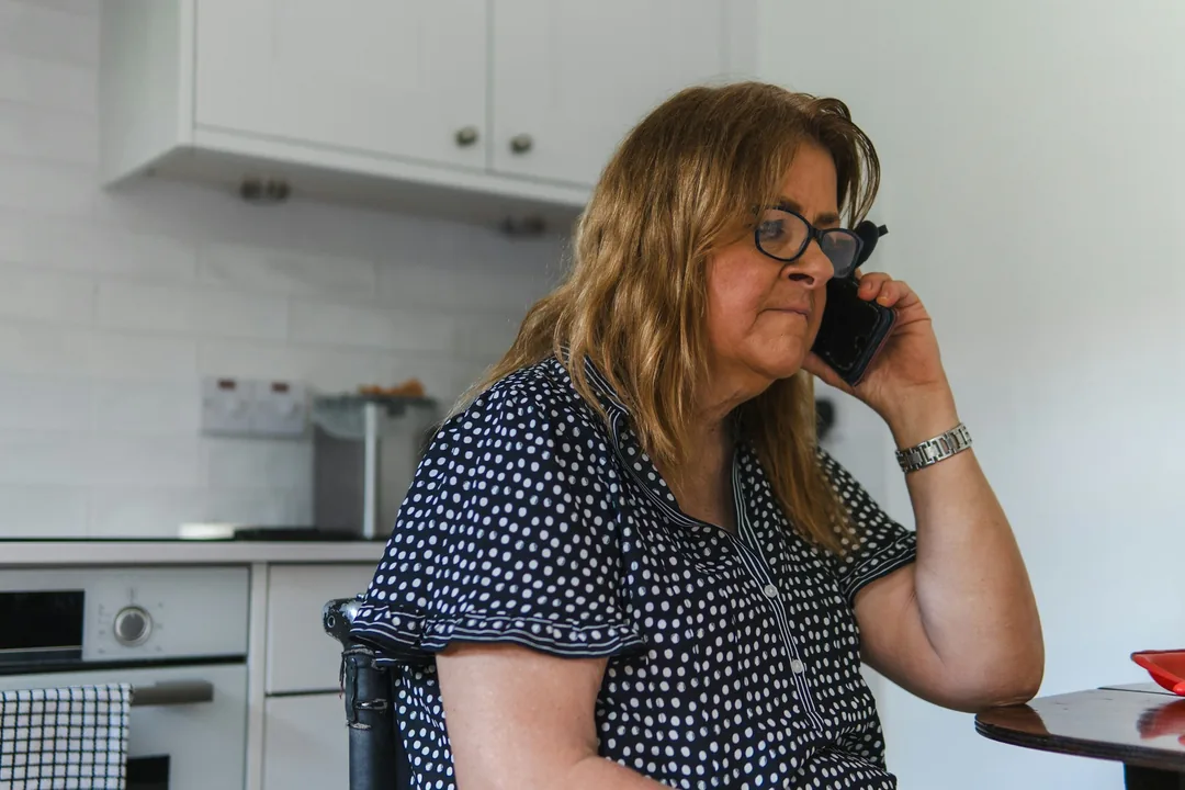 Femme au téléphone dans sa cuisine, qui appelle sa mutuelle