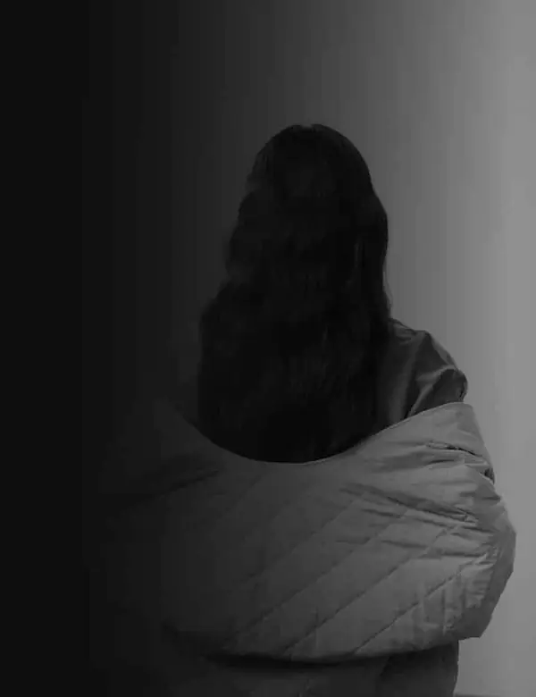 Femme de dos, enveloppée dans une veste matelassée, près d'une lumière douce
