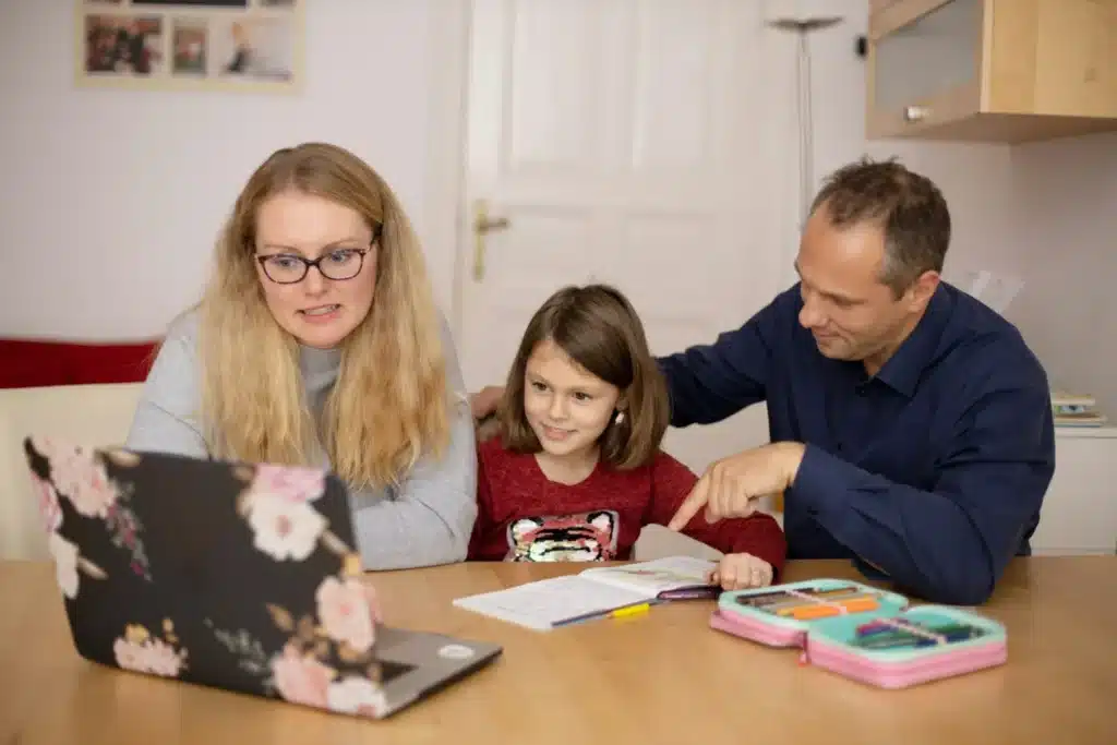 Parents assis à la table avec leur fille, un cahier et une trousse ouverts devant eux