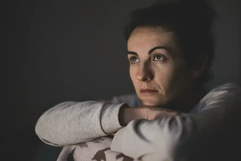 Femme au regard pensif, les bras croisés sous le menton, dans une pièce sombre