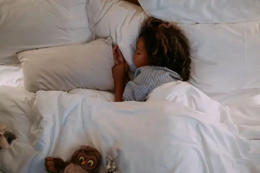 Enfant qui dort paisiblement dans un grand lit blanc
