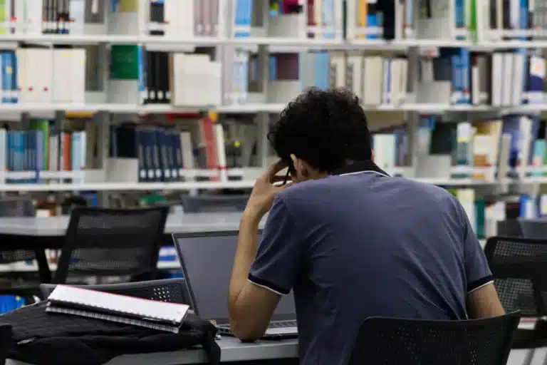 Étudiant de dos qui révise sur son ordinateur à la bibliothèque