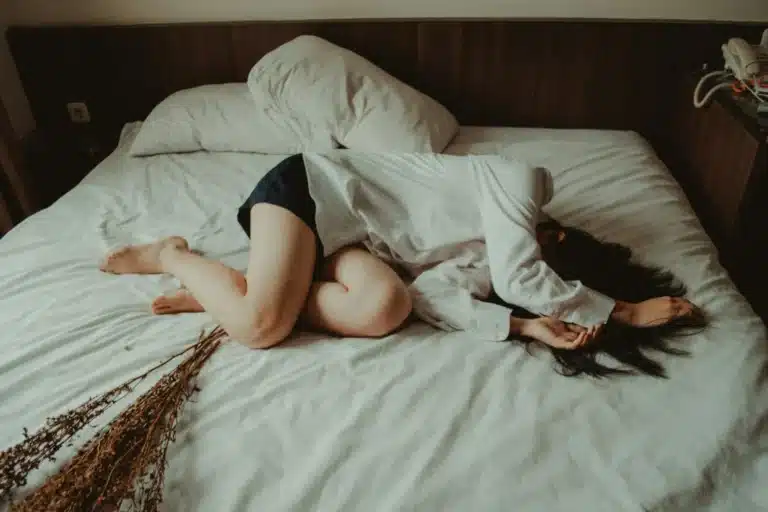 Femme allongée sur un lit défait, les jambes repliées