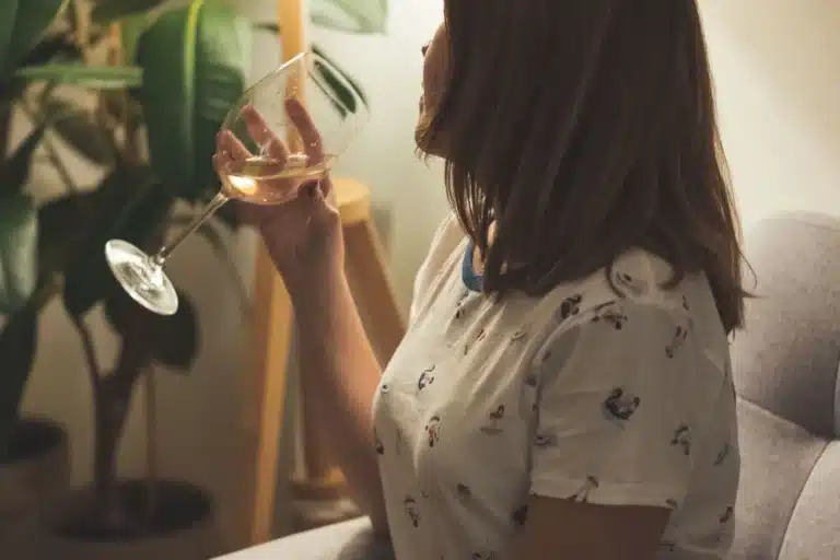 Femme qui boit un verre de vin, seule près de la fenêtre
