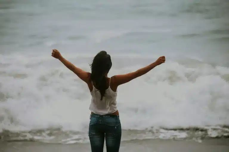 Femme de dos, les bras ouverts face aux vagues de la mer