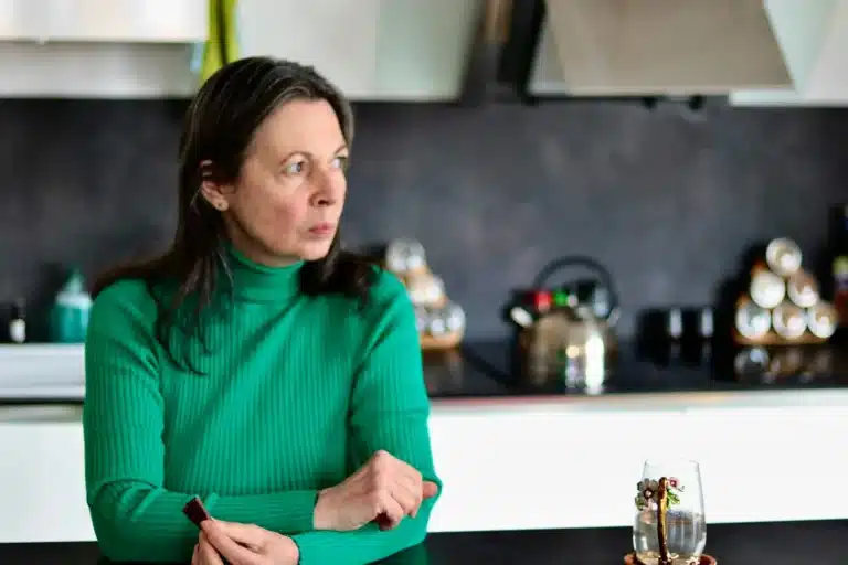 Femme d'une cinquantaine d'années, pensive, assise dans sa cuisine