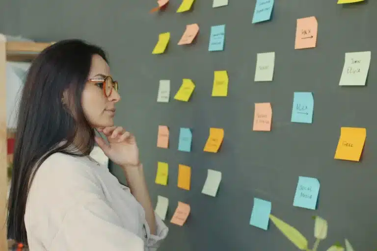 Femme pensive devant un mur couvert de post-it colorés