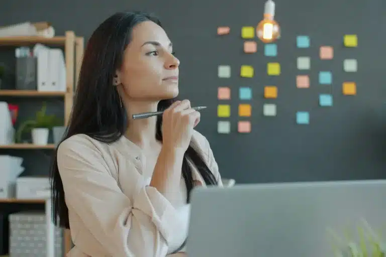 Femme pensive à son bureau, devant un mur de post-it