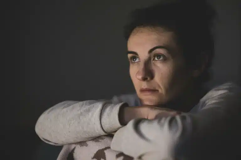 Femme pensive, les bras croisés, le regard tourné vers la fenêtre