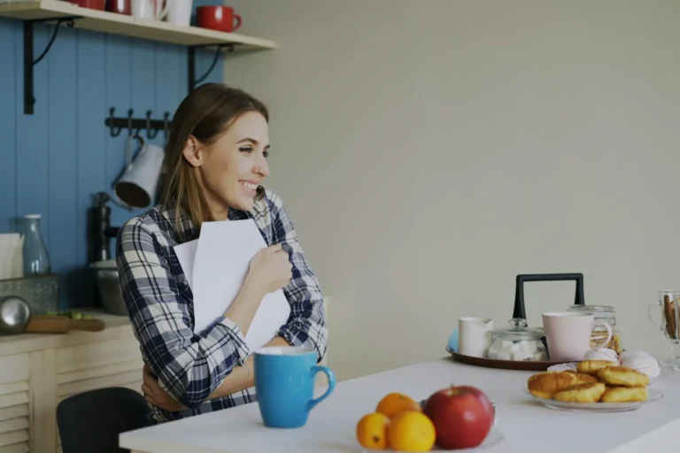 Femme souriante, un carnet à la main, dans sa cuisine le matin