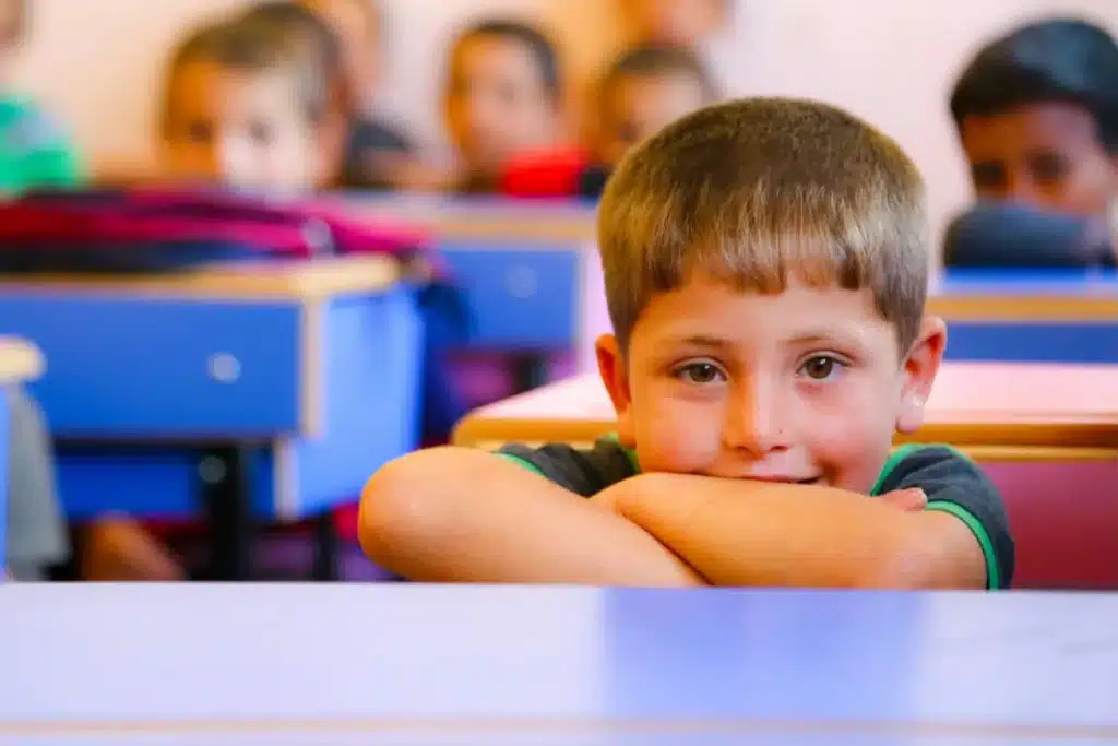Garçon souriant en classe, les bras croisés sur sa table, le jour de la rentrée
