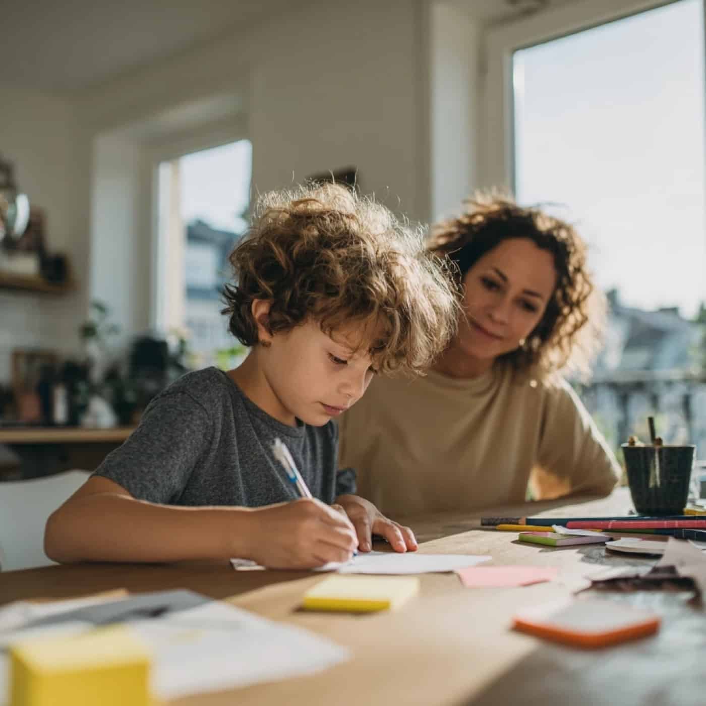 Un garçon écrit, sa mère à côté de lui, calme