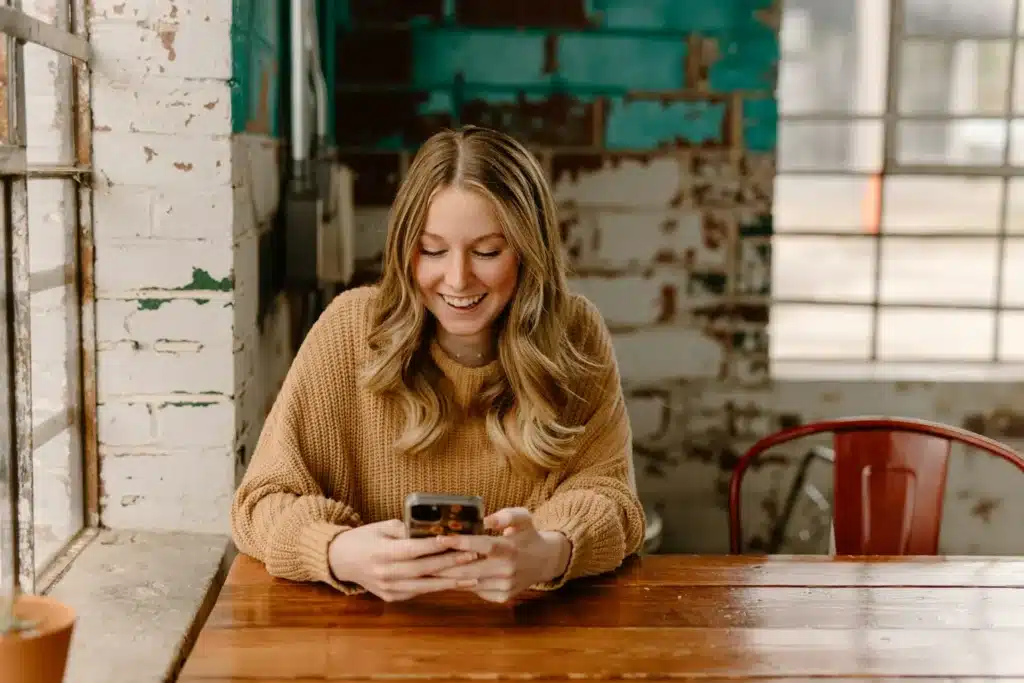 Femme assise à une table, les yeux posés sur son téléphone, dans l’attente d’un message