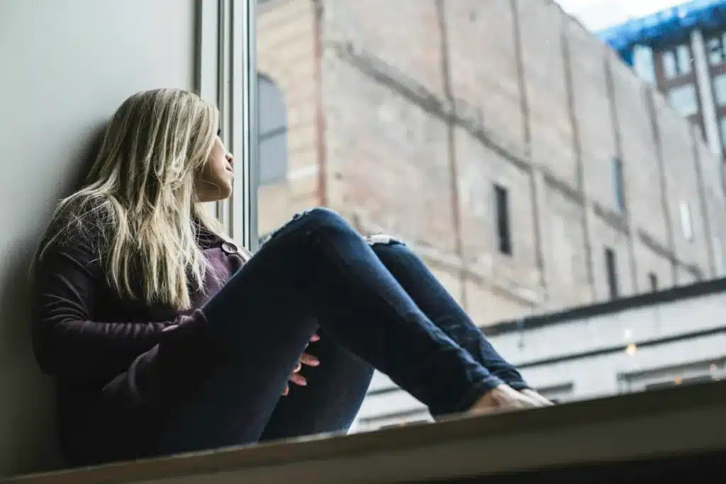 Femme assise sur le rebord d’une fenêtre, perdue dans ses pensées en regardant le ciel