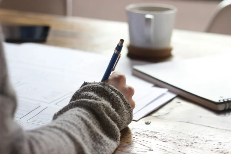 Main qui écrit une liste sur papier, à côté d'une tasse de café