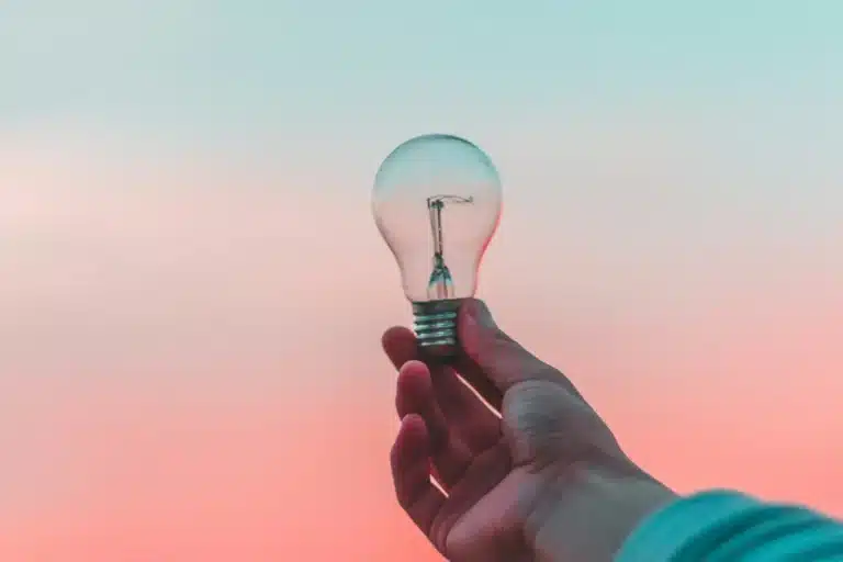 Main qui tient une ampoule devant un ciel lumineux