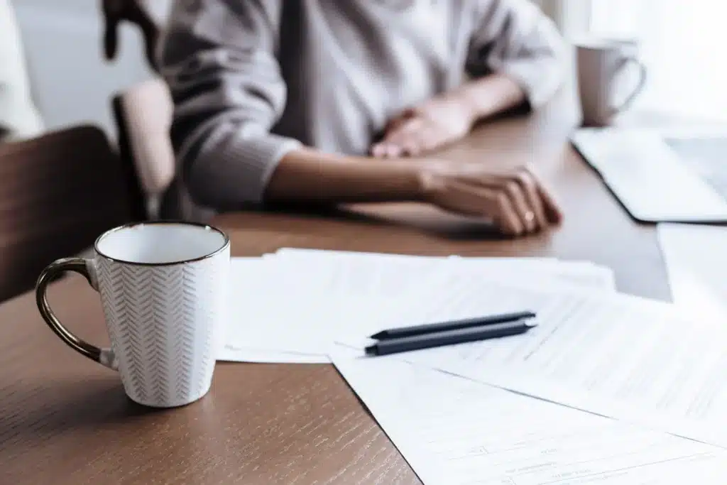 Mains posées sur des papiers administratifs, à côté d'une tasse