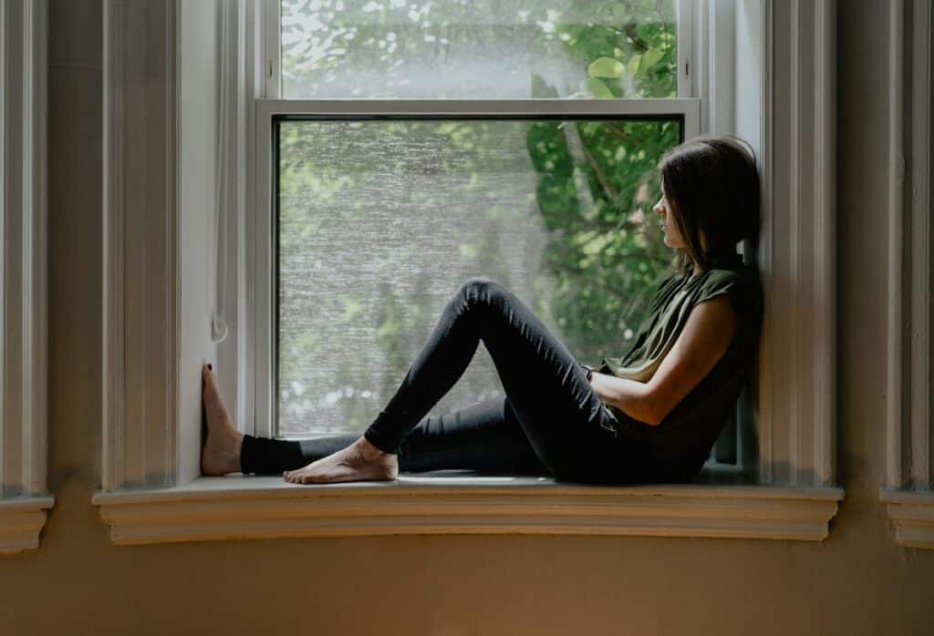 Femme assise près d'une fenêtre qui réfléchit à son fonctionnement