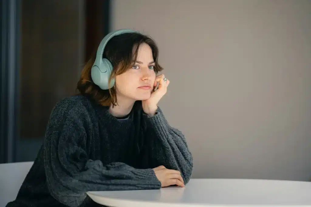Jeune femme avec un casque sur les oreilles, accoudée à une table, absorbée dans ses pensées