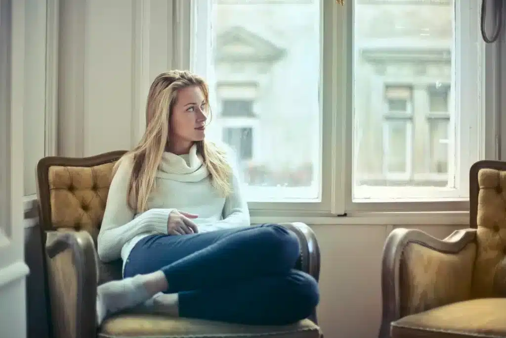 Femme installée dans un fauteuil près d’une fenêtre, les yeux tournés vers l’extérieur