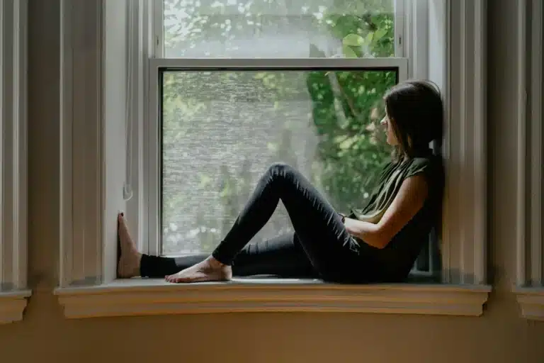 Femme assise sur le rebord d’une fenêtre, le regard perdu au loin