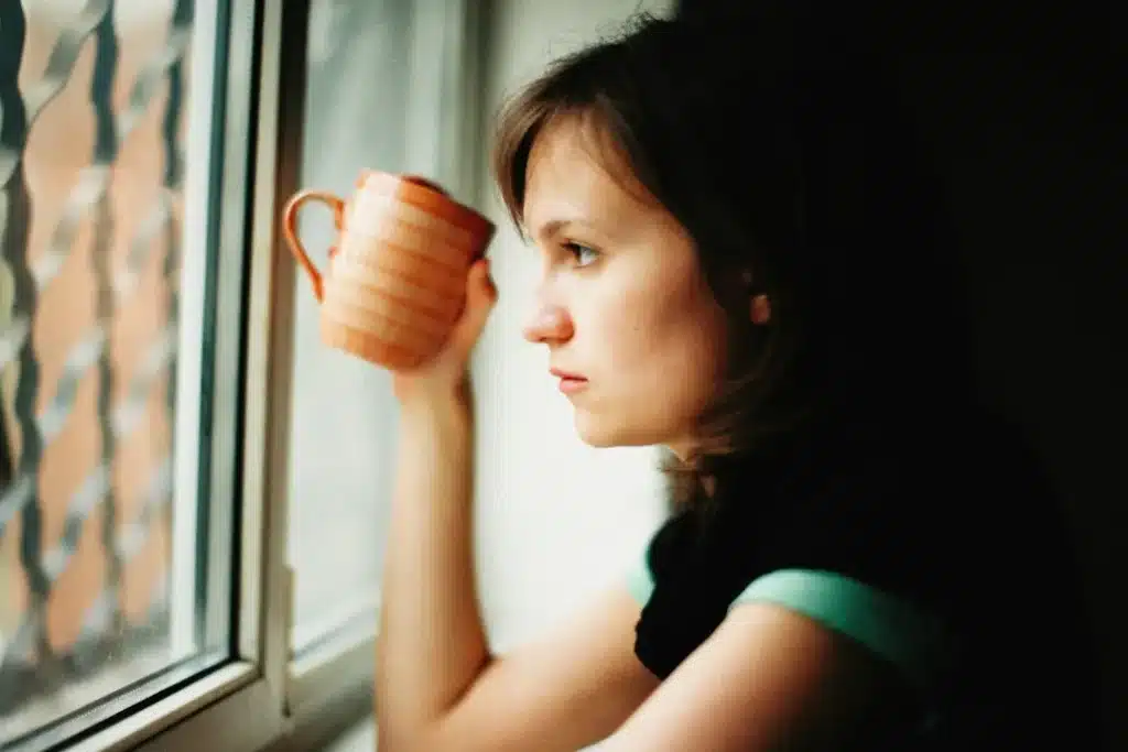 Femme pensive près d'une fenêtre, une tasse à la main