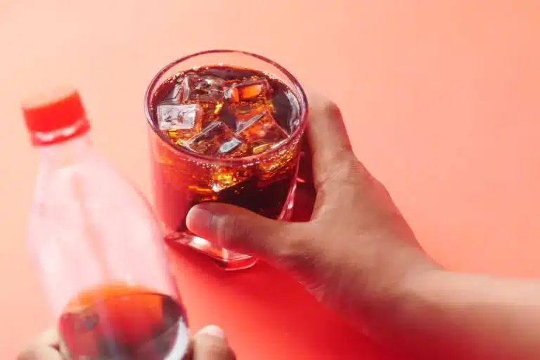 Main qui tient un verre de soda rempli de glaçons